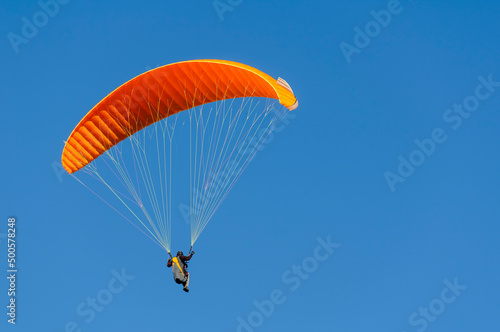 Paragliding orange flying against blue sky. Adventure sport.