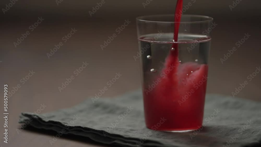 Slow motion pour berry juice in tumbler glass with water on wood table Slow motion pour berry juice in tumbler glass with water on wood table
