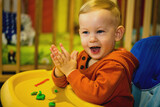 Cheerful modeling with plasticine by a little blonde boy in a highchair and smiling joyfully