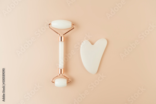 A white Guasha face massager and a face roller lying on a beige background photo