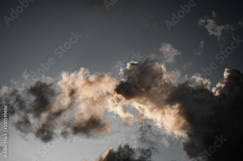 Powerfull dramatic smoke like clouds with sunset reflection and writing space, partly condensed and stormy nimbo cumulus, black and white sky at night