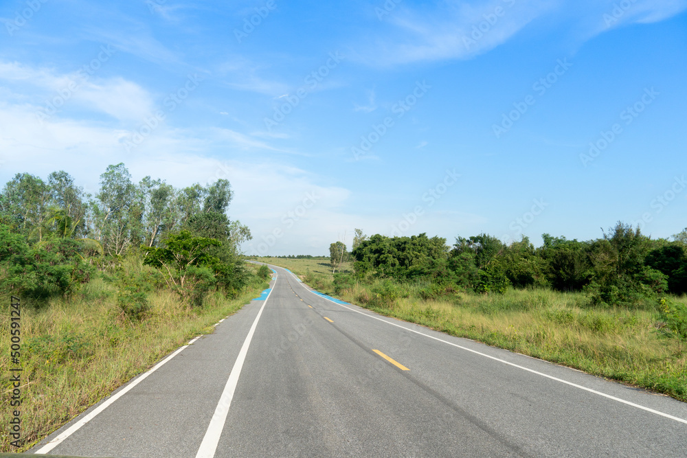 Straight path forward of Asphalt road and blue bike path shoulder road in Thailand. beside ground of green grass and trees. Under the blue sky.