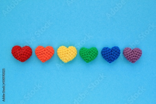 Crochet hearts rainbow colors on blue background. LGBT flag gay pride community  equal rights movement and gender equaluty concept. Valentine s Day idea for postcard  banner  poster  advertising 