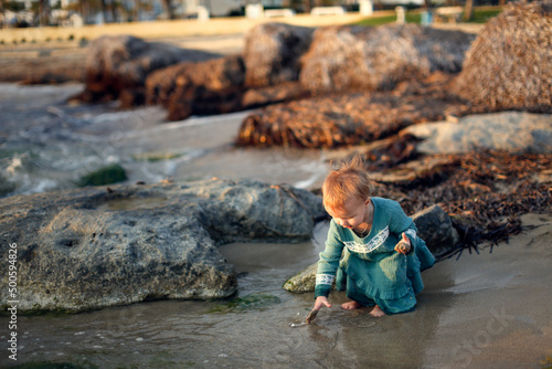 Child girl toddler in a casual dress made of muslin on the sea, a child walks along the beach near the sea, near the water