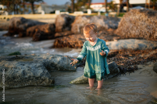 Child girl toddler in a casual dress made of muslin on the sea, a child walks along the beach near the sea, near the water