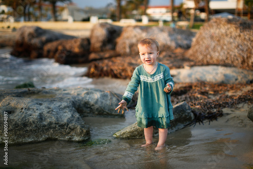Fototapeta Naklejka Na Ścianę i Meble -  Child girl toddler in a casual dress made of muslin on the sea, a child walks along the beach near the sea, near the water