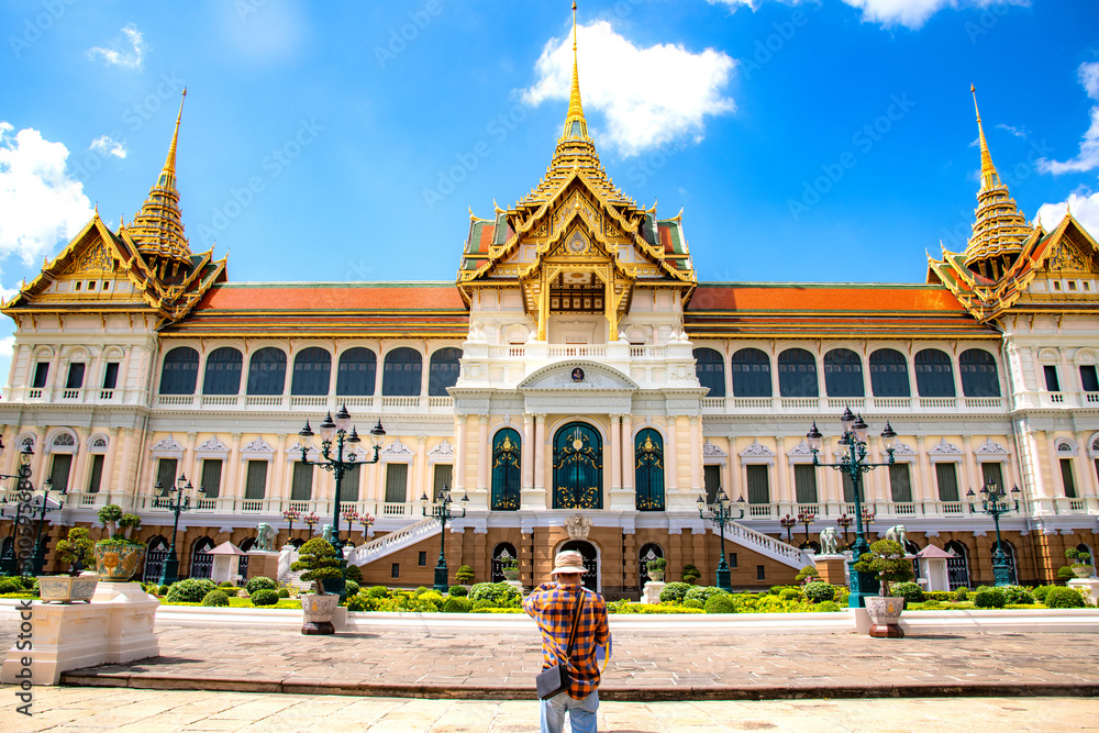 The unidentified tourist wearing the hat are looking at the beautiful building at grand palace, Wat Phra Kaew Temple of the Emerald Buddha in Bangkok.