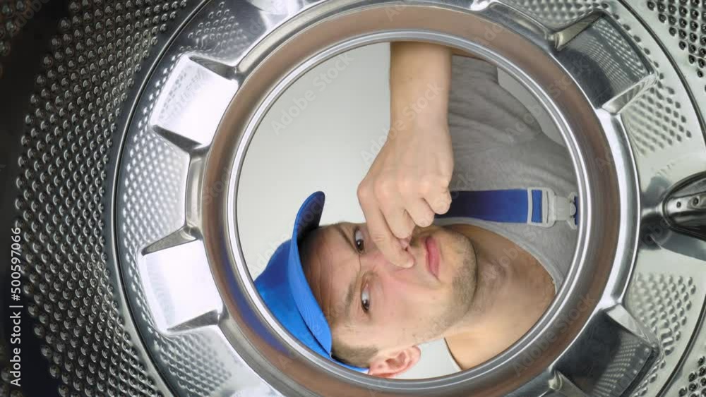 Smelly washing machine and laundry room. Master repairman looks inside washing machine, smells stench and plugs his nose. View from inside drum at wide angle. odor elimination. man. Smelly washing machine and laundry room. Master repairman looks inside washing machine, smells stench and plugs his nose. View from inside drum at wide angle. odor elimination. man.