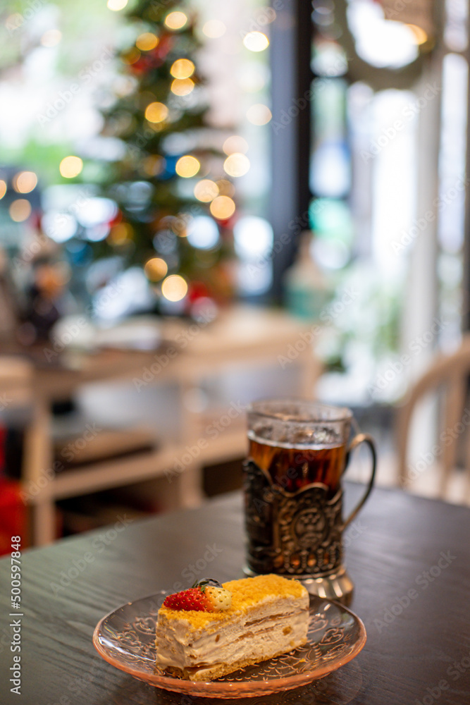 Russian Tea, A Glass in Glass Holder. With Medovik, Honey cake on the table with blurred Christmas tree on the background