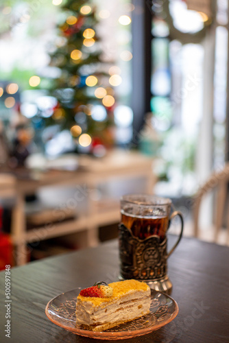 Russian Tea, A Glass in Glass Holder. With Medovik, Honey cake on the table with blurred Christmas tree on the background