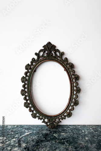 Baroque vintage metal blank frame on a white background, stands on a blue textured tabletop. Ready blank for any image.