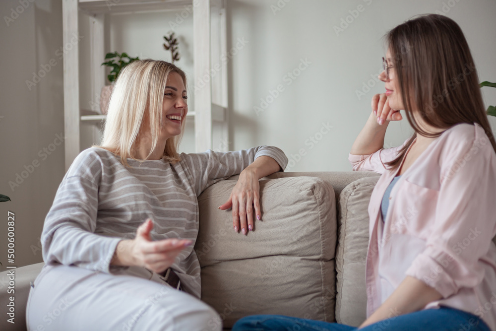 Young women friends talking, smiling together, sitting on sofa at home