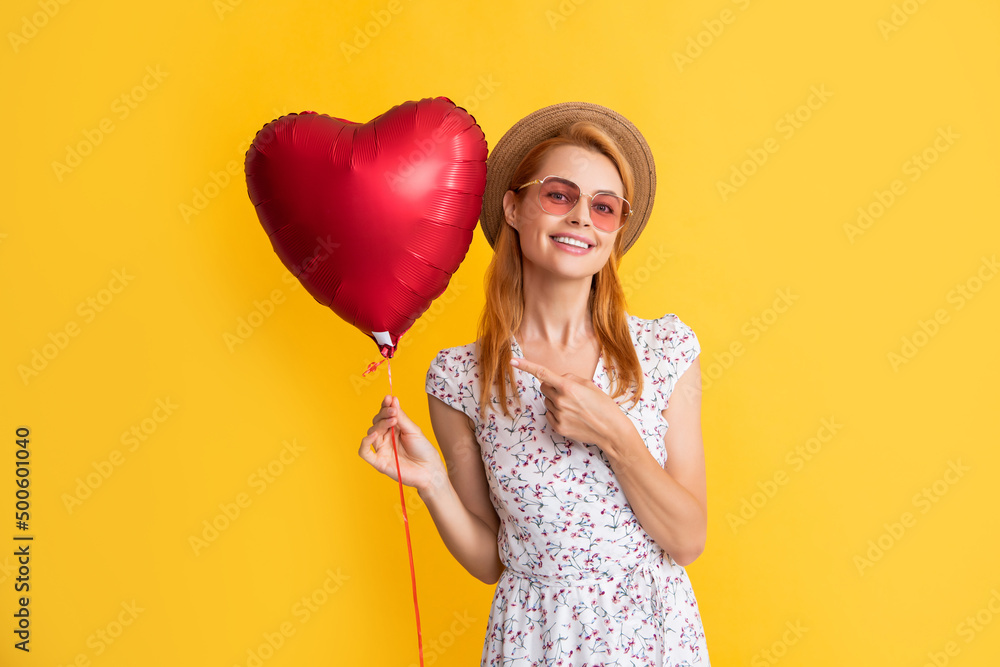 happy young woman in straw hat and sunglasses point finger love heart balloon on yellow background happy young woman in straw hat and sunglasses point finger love heart balloon on yellow background