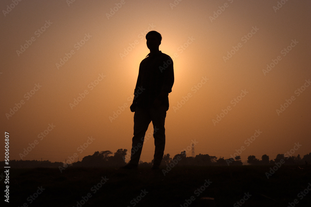 Man silhouette, standing on a rural field and looking straight. Silhouette of a man with a sunset view on a field. Nature concept with a sunset view and a boy standing silhouette close-up photography.