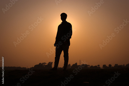 Man silhouette, standing on a rural field and looking straight. Silhouette of a man with a sunset view on a field. Nature concept with a sunset view and a boy standing silhouette close-up photography.