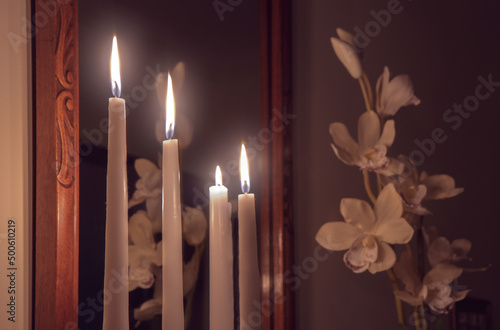 Fotografia Four lit white taper candles in front of a mirror, candlelight illuminating an o