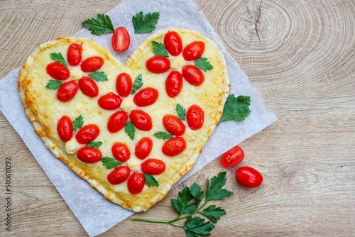 Heart shaped vegetarian Italian pizza with flower shaped tomatoes,cauliflowers and parleys on parchment paper with wooden background.Love concept for Valentine's day and Mother's day.Top view photo