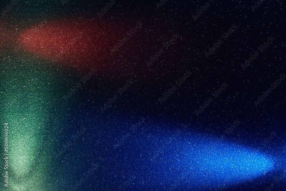 Obraz premium On a black background in fine grain, rays of blue red and turquoise light