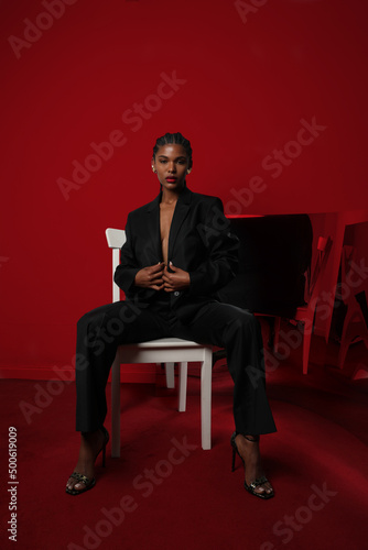 Vertical portrait of African young woman with braids wears dark suite on red.