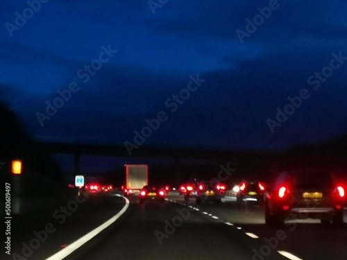 Defocused rear car lights on motorway with dark blue sky above.