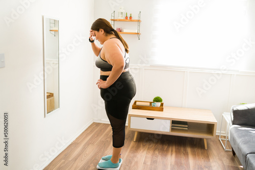 Stressed overweight woman using the weighing scale photo