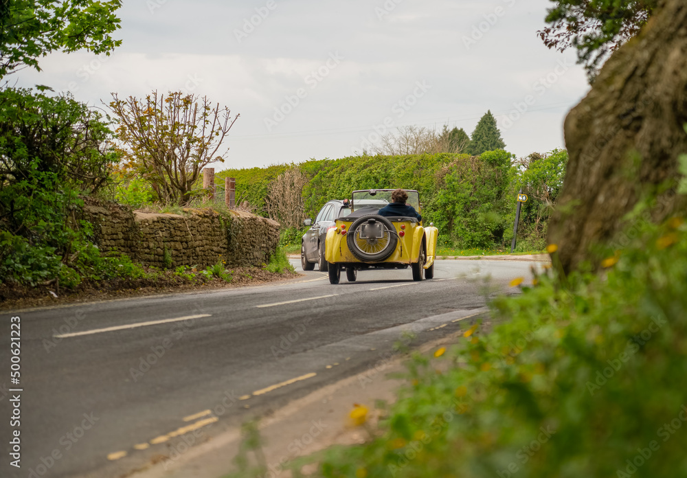 a yellow singer super 9 sports roadster automobile driving top down around a left hand bend on a country road