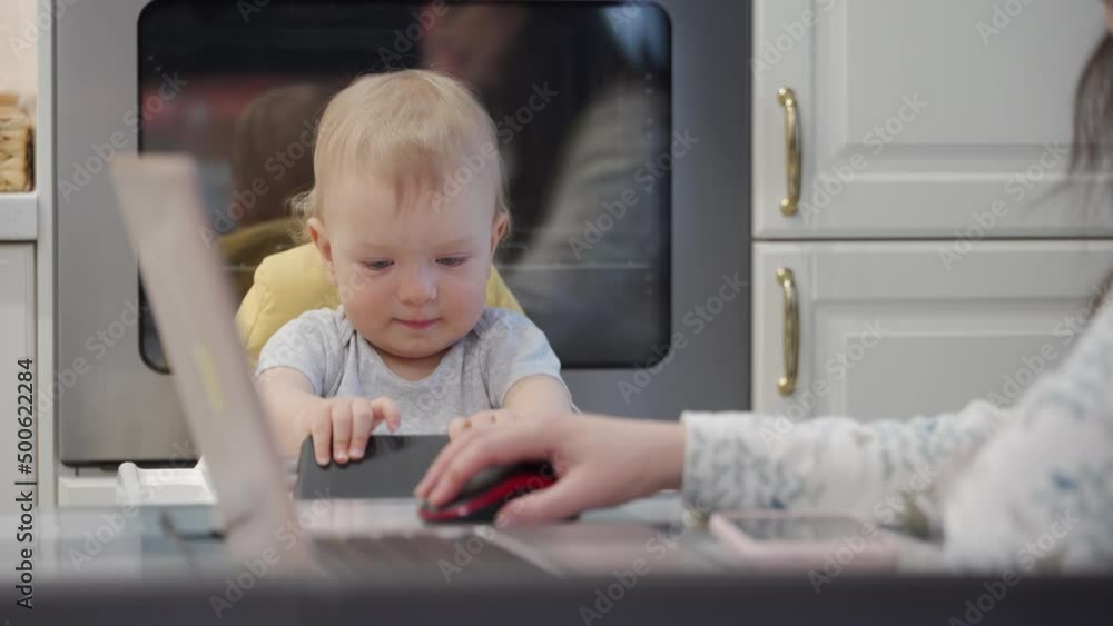 Woman with baby working at home. Mother works on laptop while her toddler playing with smartphone. Mother working and parenting. Working woman with one year old baby boy. High quality 4k footage Woman with baby working at home. Mother works on laptop while her toddler playing with smartphone. Mother working and parenting. Working woman with one year old baby boy. High quality 4k footage