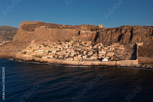 Aerial view of ancient city Monemvasia behind fortress wall on shore of island at sunrise, Greece
