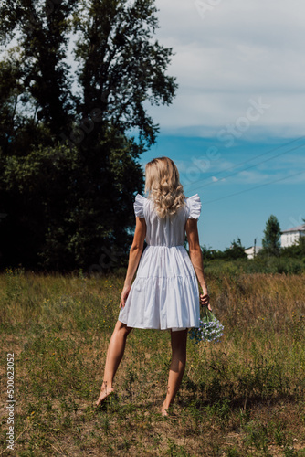 A girl in a rustic dress turned her back and holds flowers in her hand © Ирина Санжаровская