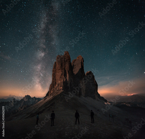 Boy, man is standing in front of moutains Tre Cime di Lavaredo in Dolomites, Italy during night with full of stars and Milky way. Amazing landscape night photo with atmosphere. 