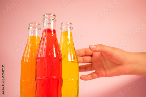 Some colorful cold soda bottles and hand taking one on pink background  photo