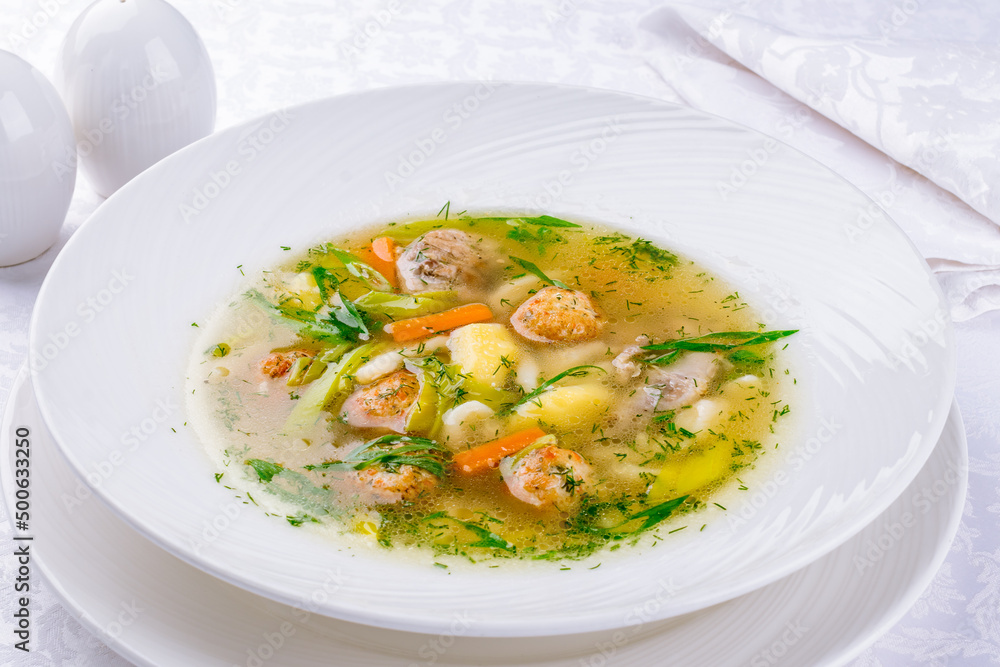 Chicken soup bouillon in a plate with chicken balls and vegetables
