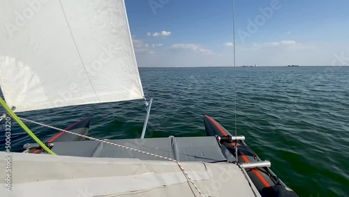 Catamaran sails along Tsimlyansk reservoir. Close-up view from deck to bow and white sails. Sunset. Movement in wind on sailing boat. Boat trip on yacht. Sports competitions on high seas. photo