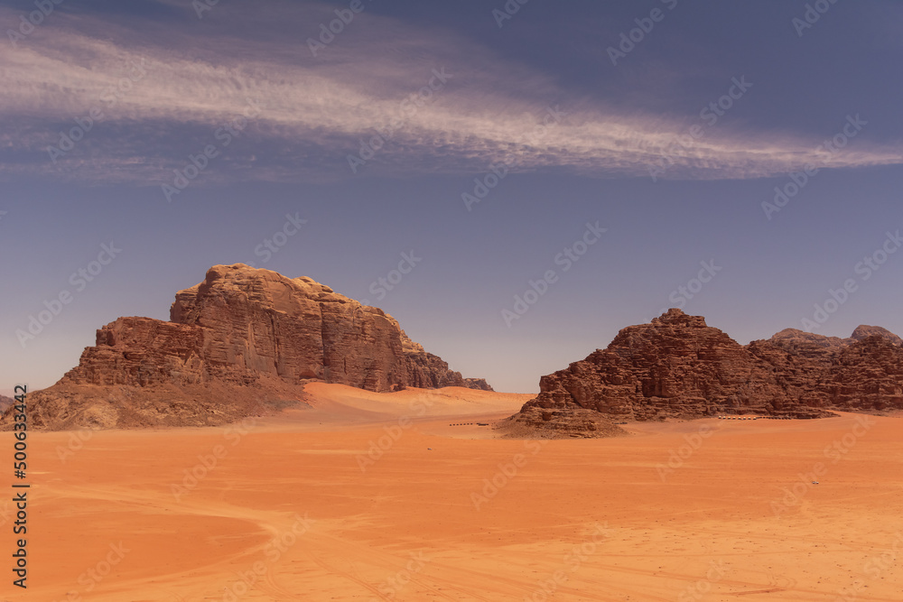 Widok pustyni Wadi Rum w Jordanii z skalistymi wzgórzami z czerwonego piaskowca i z błękitnym niebem.