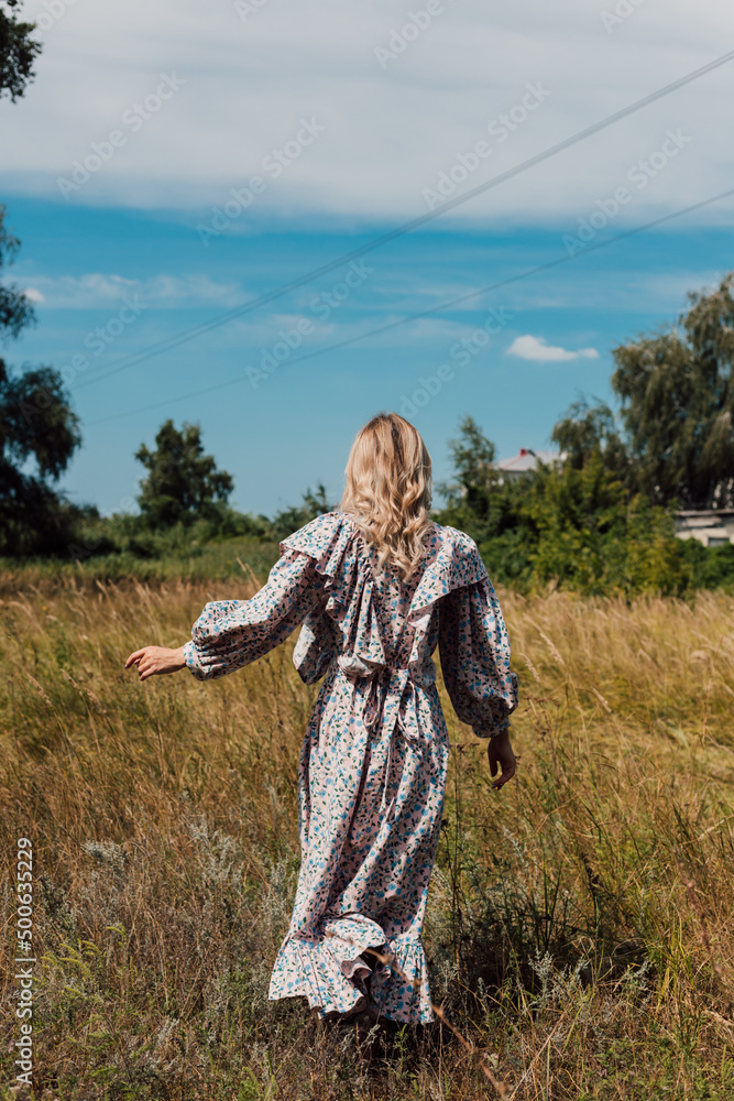 A young woman in a long country dress stands in a field with her back forward A young woman in a long country dress stands in a field with her back forward