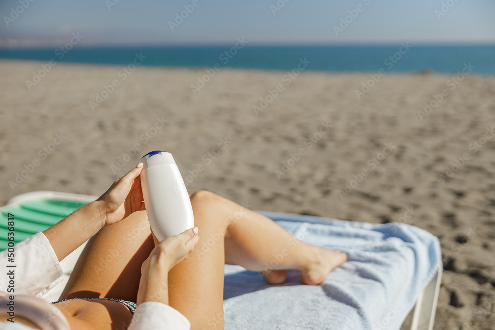 Hands of woman holding sunscreen body lotion while lying on deck chair Hands of woman holding sunscreen body lotion while lying on deck chair