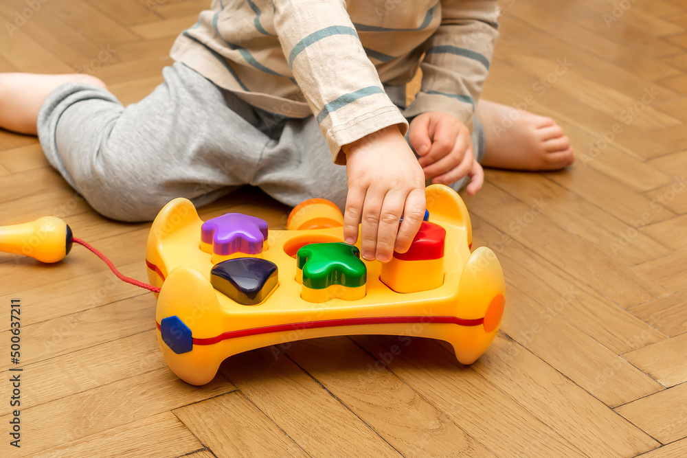 Cute little caucasian boy playing, collects multi-colored sorter constructor. Baby's hands puzzle sorter of plastic toy. Children logic development, childhood daycare education,kindergarten concept Cute little caucasian boy playing, collects multi-colored sorter constructor. Baby's hands puzzle sorter of plastic toy. Children logic development, childhood daycare education,kindergarten concept