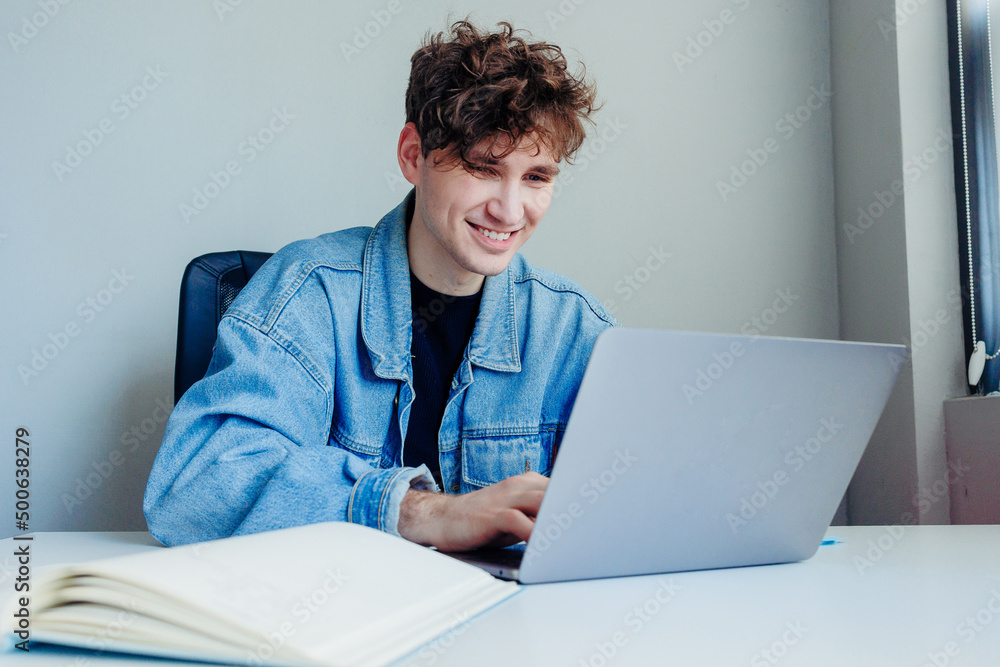 Smiling young man working on his laptop. Freelancer in the office or at home working. Smiling young man working on his laptop. Freelancer in the office or at home working.