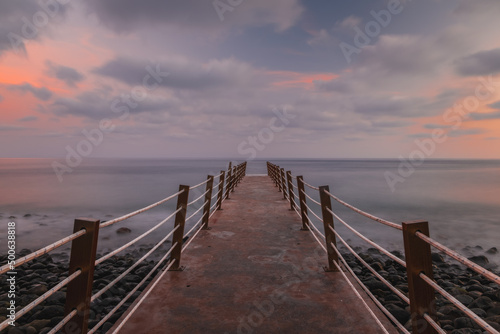 Jetty at pebbles beach near Canico at Portugese Madeira Island at sunset time. October 2021. Long exposure picture