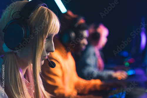 Group of online gamers, focus on the foreground. Beautiful blonde twenty-year-old gamer girl fighting in a tournament. High quality photo