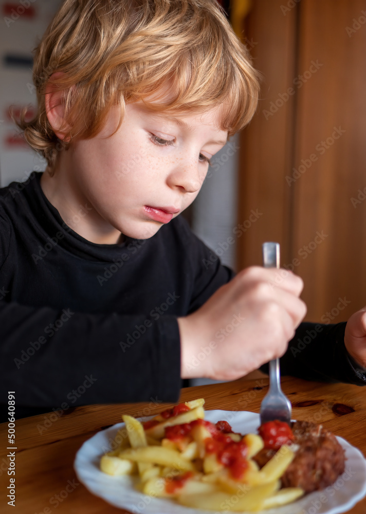 Young blond boy eats a classic meatball with french fries and ketchup Young blond boy eats a classic meatball with french fries and ketchup