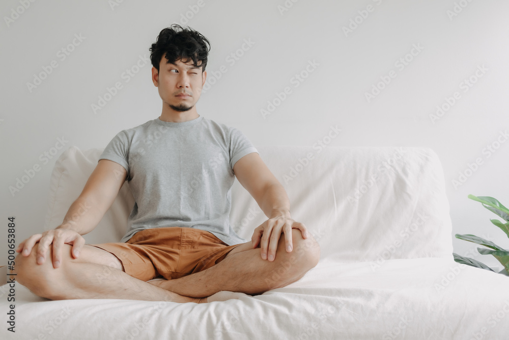 Asian man does meditation on the sofa with little distraction in his apartment. Asian man does meditation on the sofa with little distraction in his apartment.