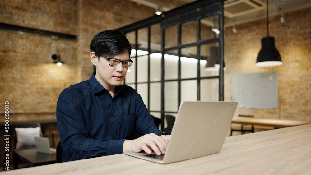 Fototapeta premium Asian businessman wearing eyeglass and working in cafe. Young handsome man working on computer laptop at workplace