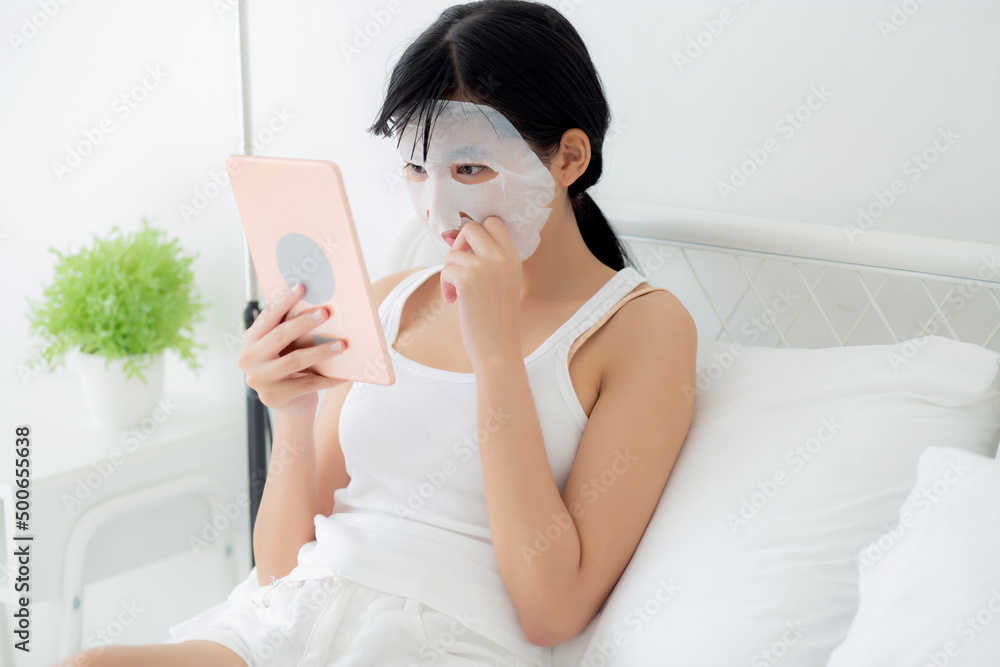 Beautiful young asian woman with sheet facial mask sitting watching tablet computer on bed at bedroom, beauty girl applying face mask for skincare of wrinkle at home, skin care, health and wellness. Beautiful young asian woman with sheet facial mask sitting watching tablet computer on bed at bedroom, beauty girl applying face mask for skincare of wrinkle at home, skin care, health and wellness.