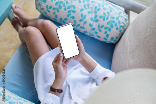 Top view mockup image of a woman holding and using mobile phone with blank desktop white screen at home