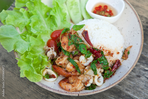 Thai Food - rice topped with Stir Fried Shrimp and Holy Basil on a wooden table.