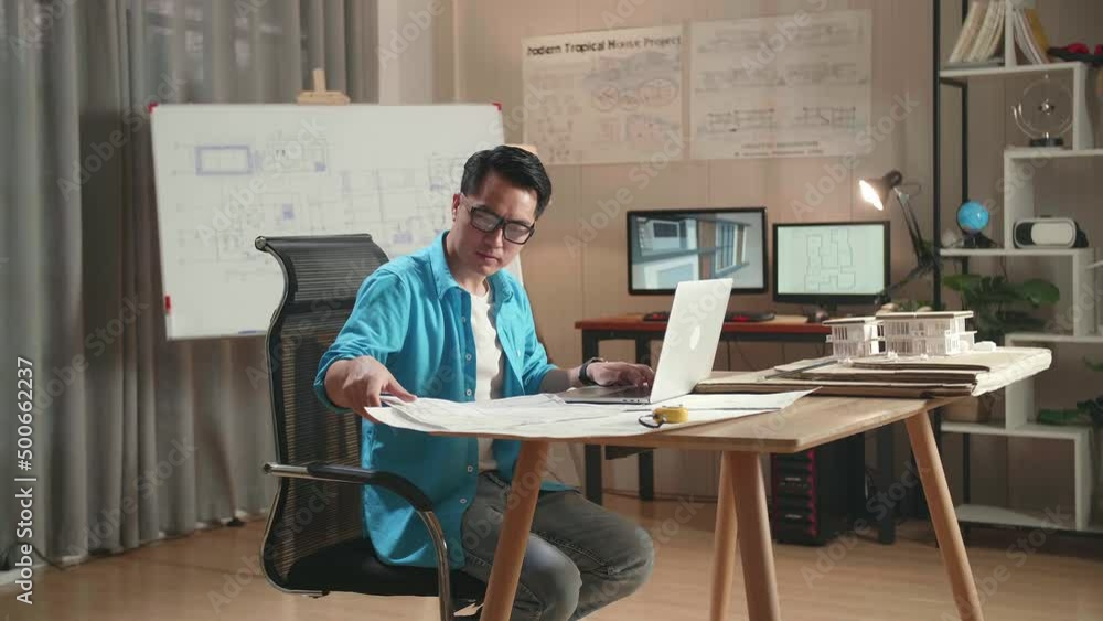 Asian Man Engineer Looking At Blueprint And Typing On A Laptop At The Office
Asian Man Engineer Looking At Blueprint And Typing On A Laptop At The Office