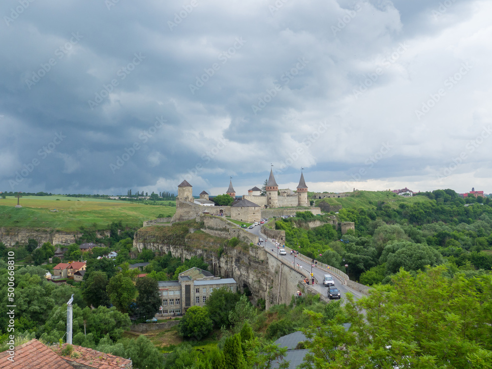 Kamianets Podilsky fortress on cloudy summer day. Scenic summer view of ancient fortress castle in Khmelnytskyi Region, Ukraine. Medieval stone large castle fortress with spiers and defensive towers.