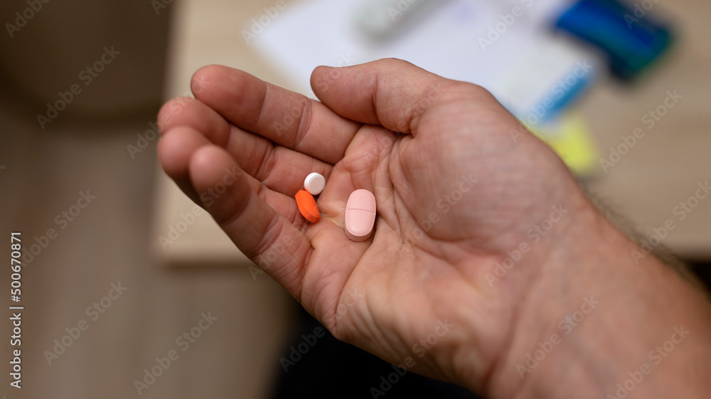 man's hand holding several pills in his hand on blur home background. Medicine and health care concept.
