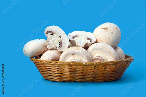 White champignons in a wicker basket on a blue background
